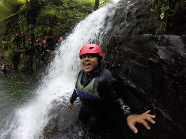 A lady gorge walking through a waterfall in South Wales