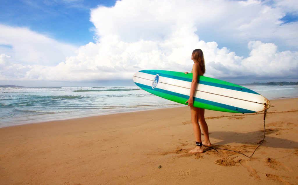 Woman holding surfboard at edge of sea
